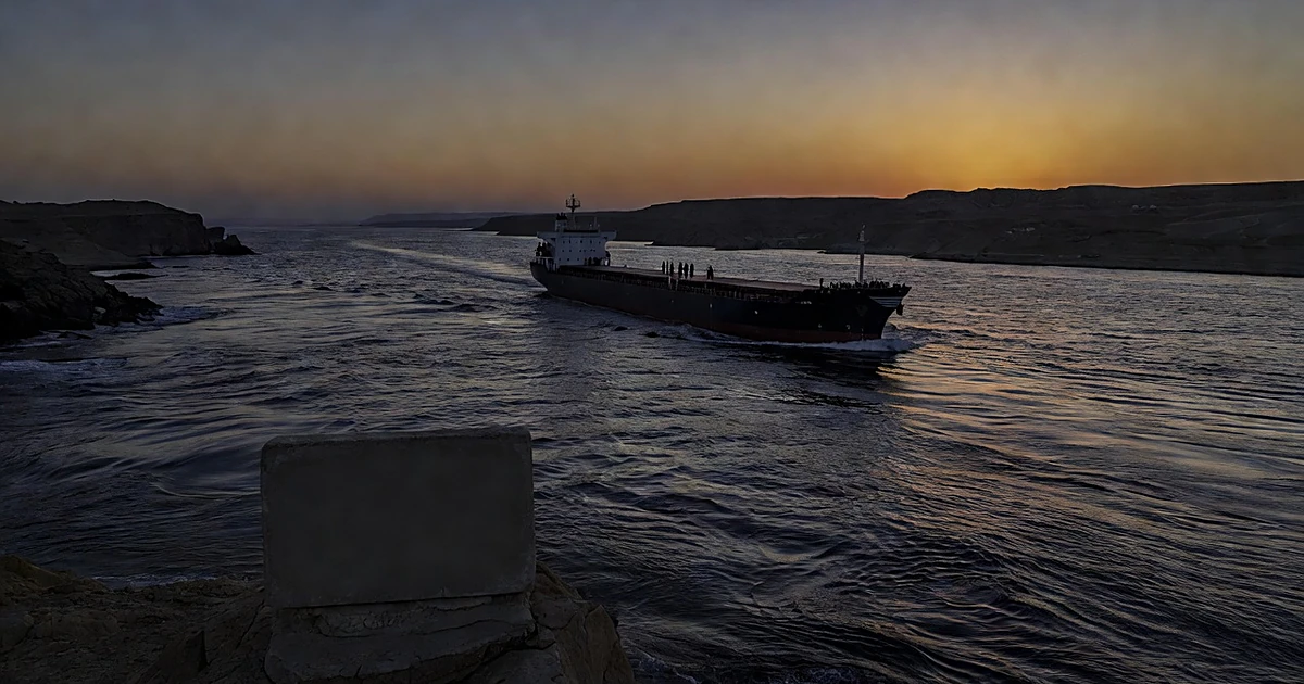 Aerial view of cargo ship passing through narrow strait at sunset with unmarked nameplate in foreground